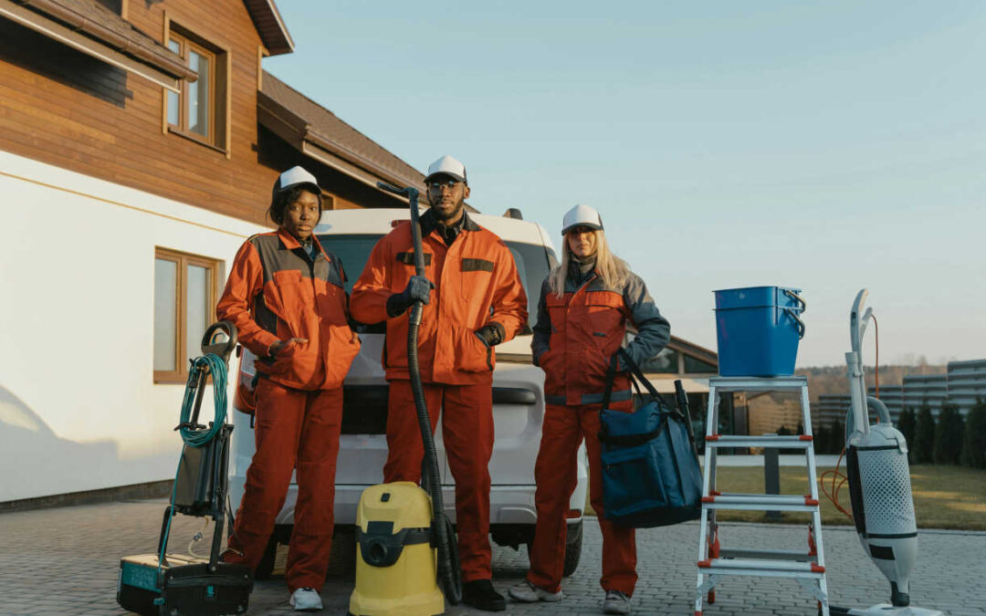 Industrial cleaning staff with vacuums, buckets, and a ladder standing outside a building.