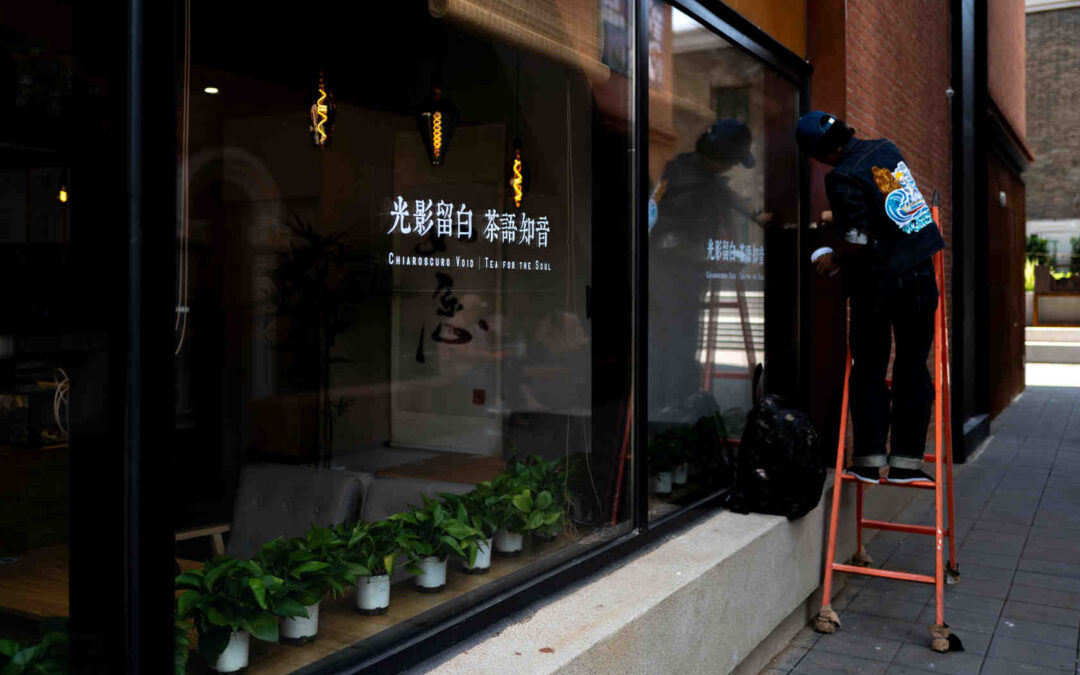 Commercial window cleaning at a storefront, technician on a ladder washing glass.
