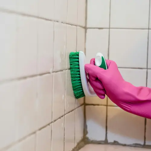 Advanced grout cleaning showing a hand scrubbing stained bathroom tile grout with a cleaning brush.